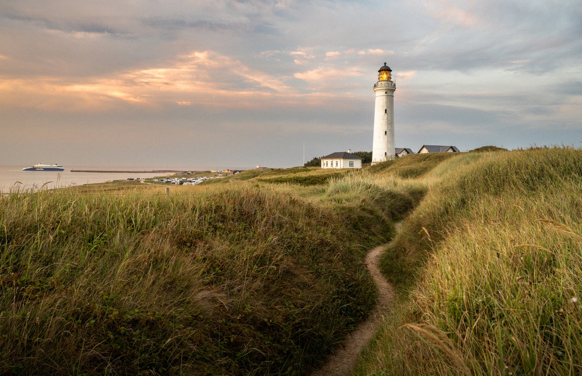 Leuchtturm Hirtshals Fyr in den Dünen, im Hintergrund eine Fähre auf der Nordsee